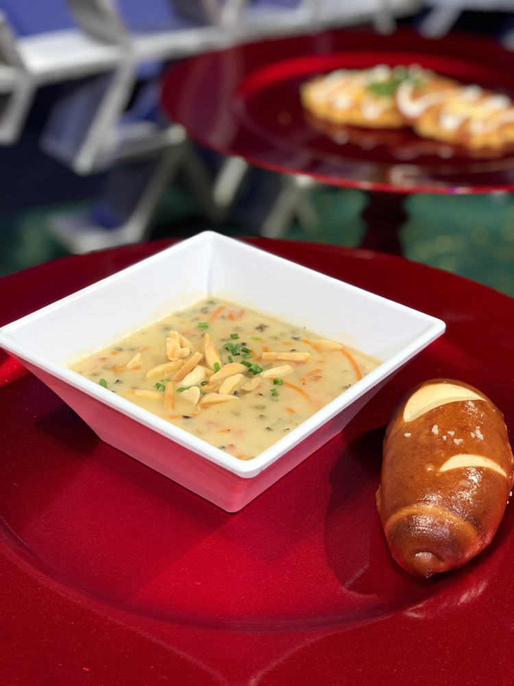 White square bowl with ham soup and a pretzel roll on a red plate